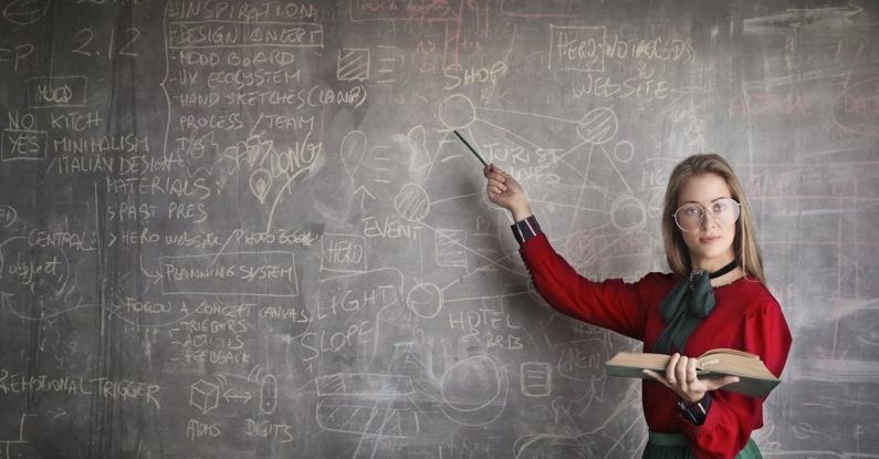 Quantum Physics - Serious female teacher wearing old fashioned dress and eyeglasses standing with book while pointing at chalkboard with schemes and looking at camera